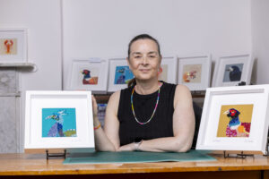 Jane Packard Artists sitting in her studio with a piece of artwork either side of her.