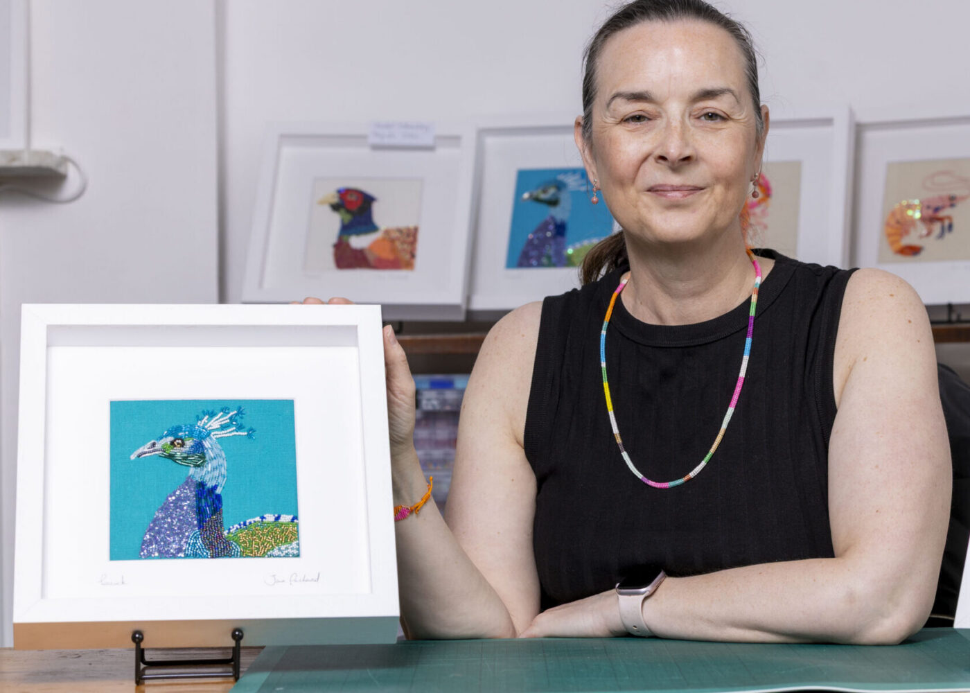 Jane Packard Artists sitting in her studio with a piece of artwork either side of her.