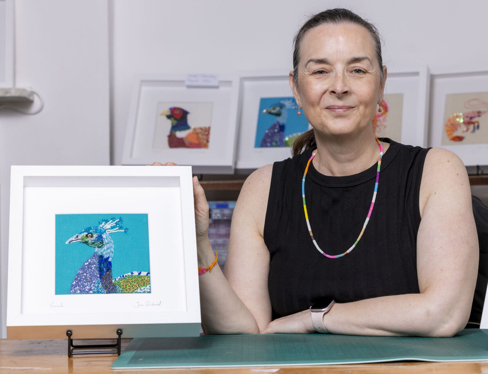 Jane Packard Artists sitting in her studio with a piece of artwork either side of her.